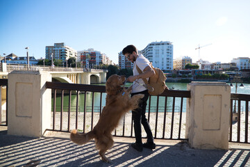 A handsome young man with his brown golden retriever dog leaning on the railing overlooking the river. They are on holiday in seville, spain. Concept pets, animals, dogs, pet love, travel.