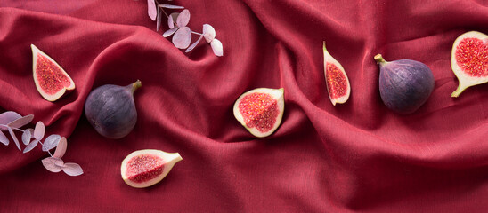 Fresh halved fig fruits and dry euvalyptus on vine red silk textile background. Panoramic banner...