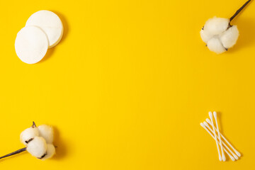 A stack of cotton pads, a stick and cotton flowers are placed around the edges of a yellow background. Place for advertising text on the poster.