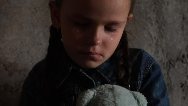 Close-up image of sad crying girl on gray wall crying and hugging teddy bear. Orphan. 