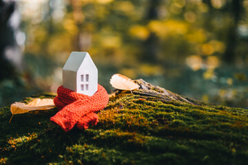 Miniature house in a red scarf on an autumn background with moss and yellow leaves. The concept of...