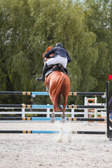 A young rider on sorrel horse jumps over an obstacle at a show jumping competition. Equestrian...