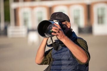 Reportage photographer with a large telephoto lens. Male photojournalist and reporter taking pictures. Focus on the lens.
