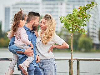 Man and woman with child outdoors. Father holding adorable child while spending time with family in new urban district.