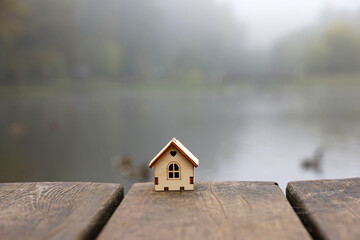 Wooden house model on boards on blurred background of autumn lake with swimming ducks in fog....