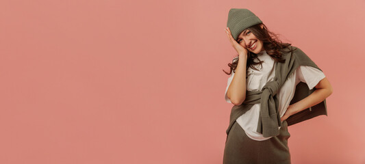 Happy young caucasian brunette girl smiles with her teeth looking at camera on pink background. Model wears white T-shirt, grey hat and sweatshirt. Lifestyle, feminine beauty concept