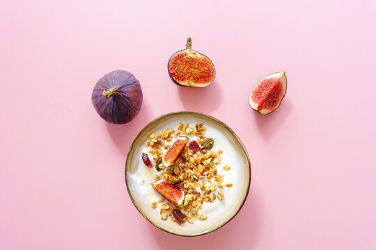Eine Fr&uuml;hst&uuml;ck Sch&uuml;ssel mit Granola, Joghurt und Feigen auf einem rosa Hintergrund. Draufsicht, minimalistisch.