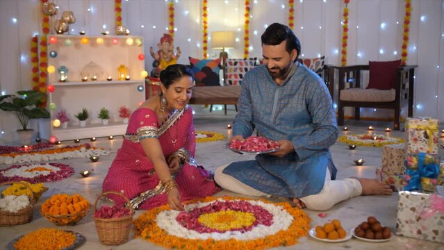 A middle-aged Indian couple is decorating a floral Rangoli with rose petals for Diwali. An Indian husband-wife duo posing for the camera - traditional wear  festive mood  family affair  auspicious ...