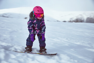 Little girl snowboarder on empty track at ski resort in sunny winter day. Portrait of kid in...