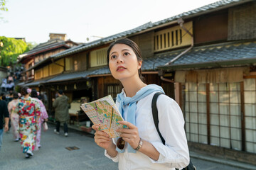 curious asian japanese female tourist looking up at sky to check weather while consulting guide map at Ninenzaka and Sannenzaka in Kyoto japan with a group of kimono girls at background