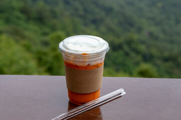 Close up photo of iced milk tea in plastic glass on table and blurred nature background.