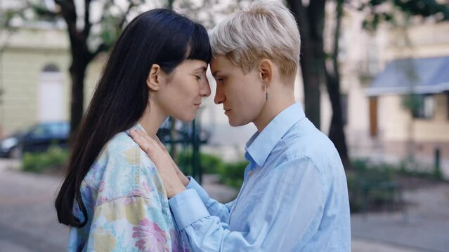 Two lesbian woman, standing in the city centre, one partner kissing her girlfriend in the forehead. Lesbian couple feeling in love together. Romantic date, love, tender relationship