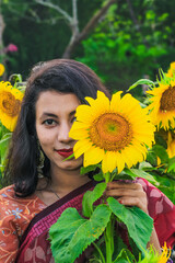 Beautiful young girl enjoying nature on the field of sunflowers. Girl in the field of sunflowers. Girl in a park smiling and covering face with sunflower.