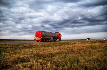 Obraz premium New red truck with a tanker truck transports gasoline against the background of the cloudy sky in the evening. Dangerous goods transport industry