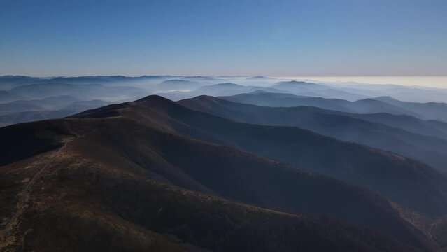 Scenic aerial view of Carpathians in early autumn, drone flies forwards over mountain range covered with morning fog on the horizon