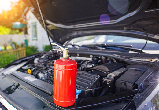 A car powder fire extinguisher is in a car with an open hood. The concept of modern fire extinguishers for extinguishing a fire in a car. Copy space for text