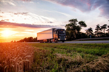 Fototapeta premium A black truck tractor transports cargo against the backdrop of a field and sunset in the evening. Profitable rate of road freight transport and freight turnover, statistics
