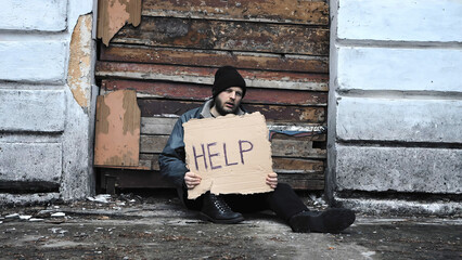 Homeless man sits and holds piece of cardboard with inscription Help. Refugee looking for job. Male...