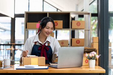 Shipping shopping online, owner writing address on cardboard box at workplace. small business entrepreneur SME or freelance asian woman working with box at home