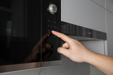 A man presses his finger on the touch panel of a microwave oven to turn on the defrost function....