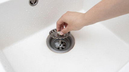 A man's hand removes a metal strainer from a kitchen sink drain. Cleaning the drain and pipes from...