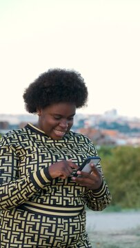 Young Equatoguinean woman laughing while using the smartphone at street.