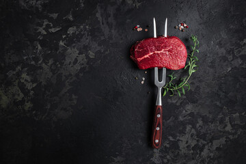 raw beef steak on a fork with rosemary and spices on a dark background. Culinary, cooking, concept....