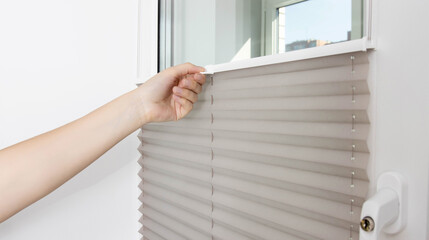 A man opens the blinds on the window to let sunlight into the room. Aluminum classic blinds with scaffold fixing system. Close-up