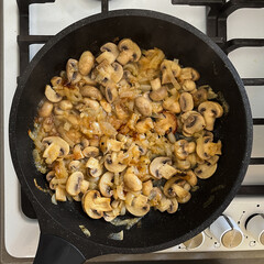 White champignon mushrooms are fried with onions in a frying pan.