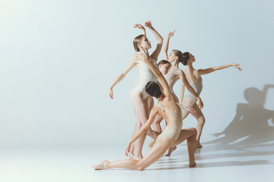 Group of young women, ballerinas dancing, performing isolated over grey studio background. Tenderness, attraction, grace