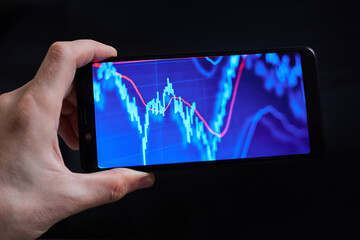 Trader analyzes stock market data in smartphone on dark background