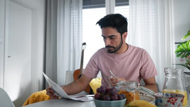 Young man drinking orange juice and reading newspaper, morning routine concept.