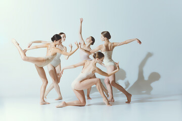 Group of young girls, ballerinas dancing, performing isolated over grey studio background. Adorable dance style