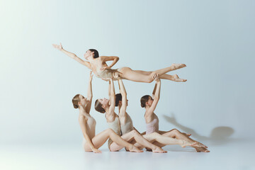 Group of young girls, ballet dancers performing, posing isolated over grey studio background. Giving support