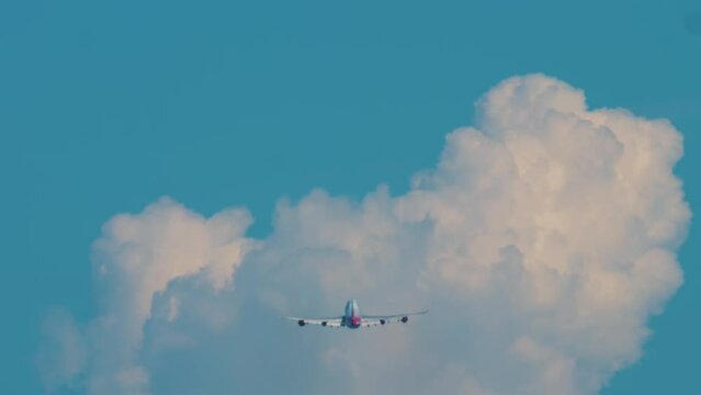 Long shot rear view of a huge wide-body four-engine aircraft climbing after takeoff. Airliner in the blue sky against the background of a white cloud