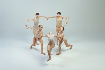 Group of young girls, ballet dancers performing, posing isolated over grey studio background. Heart...