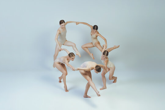 Group of young girls, ballet dancers performing, posing isolated over grey studio background. Dancing in a cricle