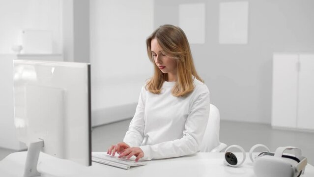 Young woman in white clothes working on computer in white office