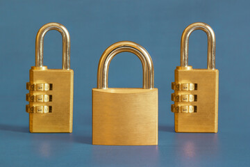 Naklejka premium A golden square padlock escorted by two rectangular combination padlocks s in the background on a blue-painted study table. Leadership and security concept..