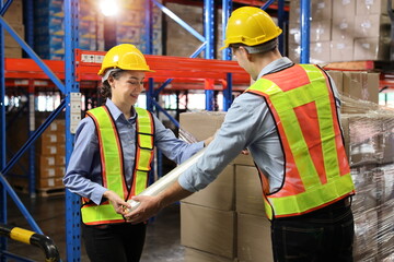 Group of warehouse workers with hardhats and reflective jackets wrapping boxes in stretch film parcel on pallet while control stock and inventory in retail warehouse logistics distribution center