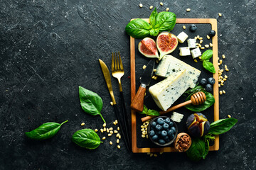 Sliced cheese on a board. Blue cheese, figs, blueberries and honey. On a concrete background. Top view.