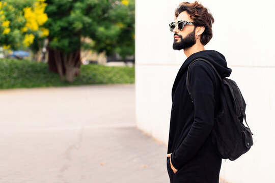 beautiful young man with backpack and fashionable sunglasses walking by the city, concept of urban lifestyle and stylish clothing, copy space for text