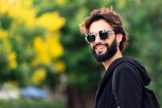 portrait of a beautiful young man with beard and fashionable sunglasses smiling happy, concept of urban lifestyle and stylish clothing, copy space for text