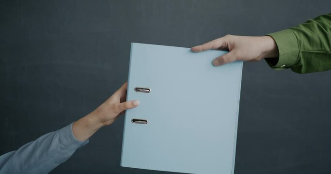 Close-up slow motion of male hand giving paper folder to female against black color background. Office supplies and cooperation concept.
