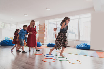 Small nursery school children with female teacher on floor indoors in classroom, doing exercise....