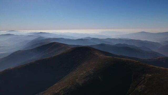 Scenic aerial view of the Carpathians range in early autumn, drone flies forwards over mountain which are covered with morning fog on the horizon