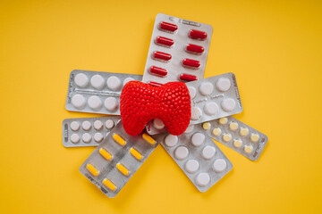 Red thyroid gland and pills on a yellow background