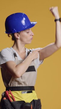 Vertical video: Strong empowered woman flexing arm muscles in studio, preparing to work on construction refurbishment with tools. Confident powerful handywoman pointing at biceps and triceps.