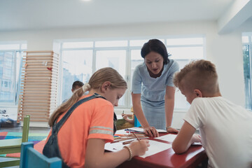 Fototapeta premium Creative kids during an art class in a daycare center or elementary school classroom drawing with female teacher. 