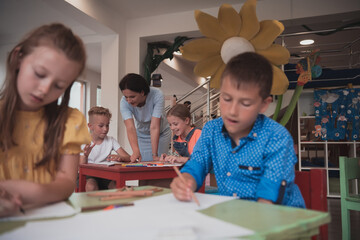 Creative kids during an art class in a daycare center or elementary school classroom drawing with female teacher. 